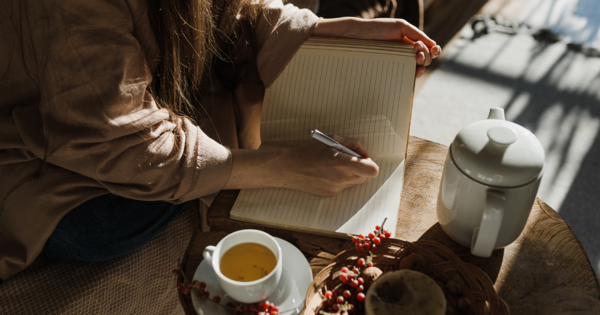 Person journaling with tea, considering microdosing coaching vs. therapy